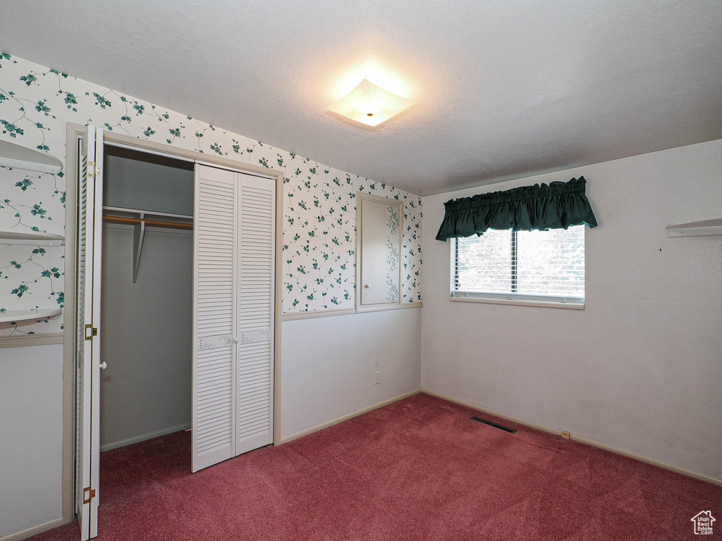Unfurnished bedroom with carpet flooring, a closet, wallpapered walls, and baseboards