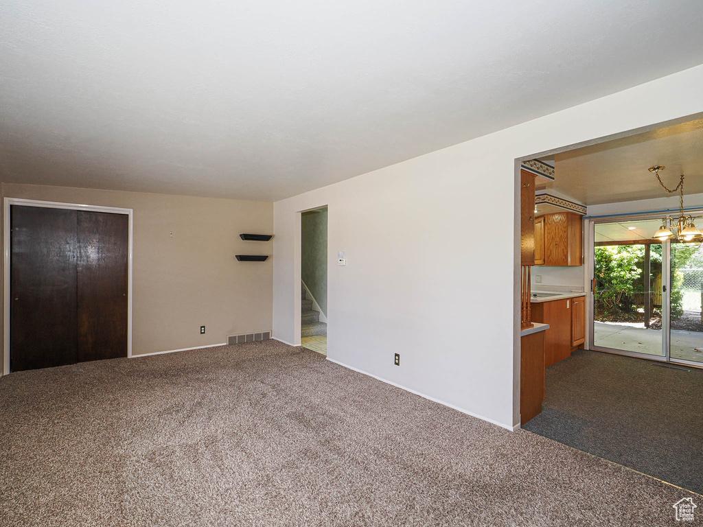 Unfurnished living room with dark colored carpet, baseboards, and stairway