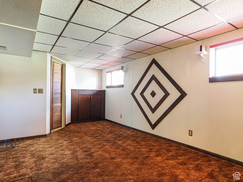 Basement featuring dark colored carpet, a drop ceiling, and baseboards