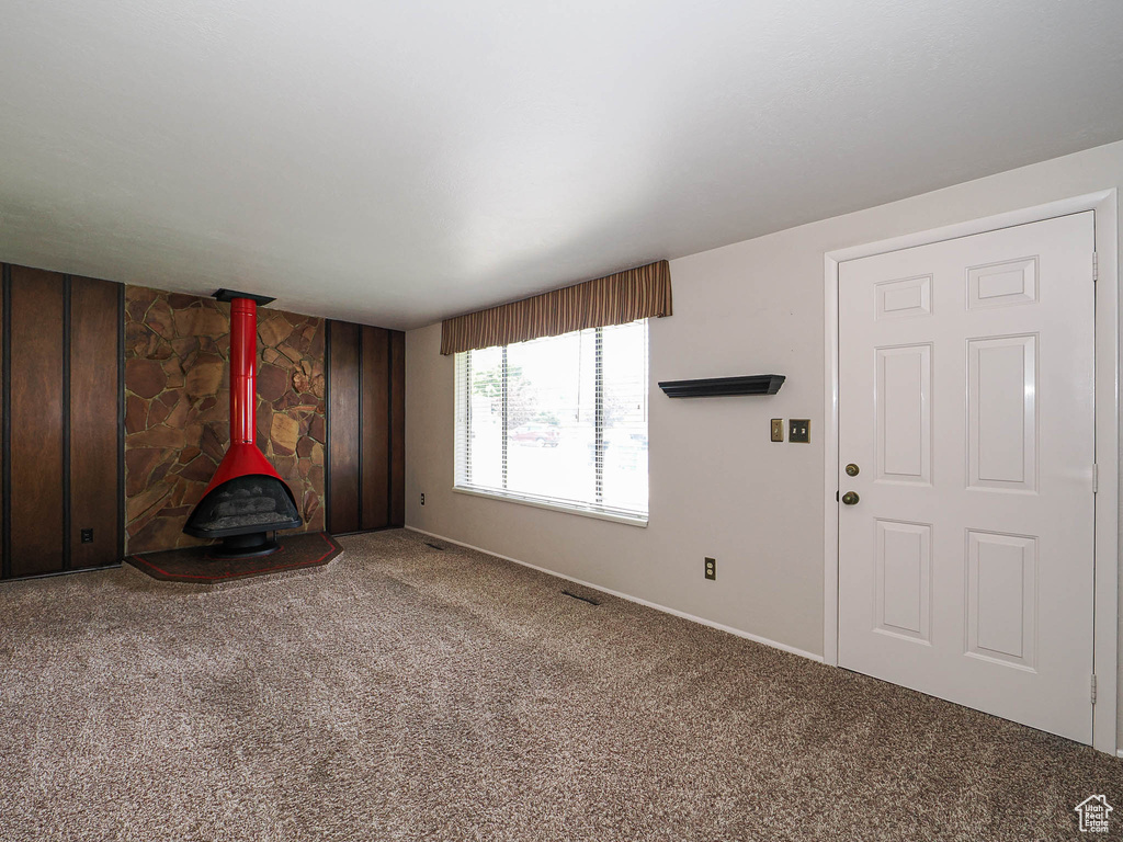 Unfurnished living room featuring a wood stove, carpet floors, and baseboards