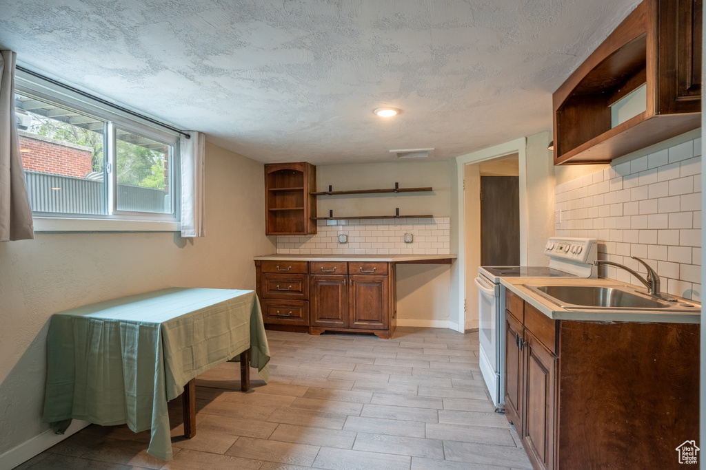 Kitchen featuring open shelves, white electric stove, a sink, and tasteful backsplash