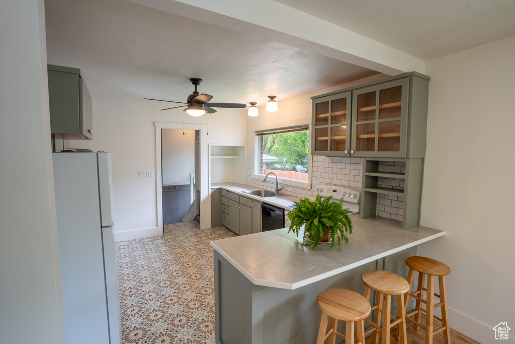 Kitchen featuring freestanding refrigerator, a sink, gray cabinetry, a peninsula, and baseboards
