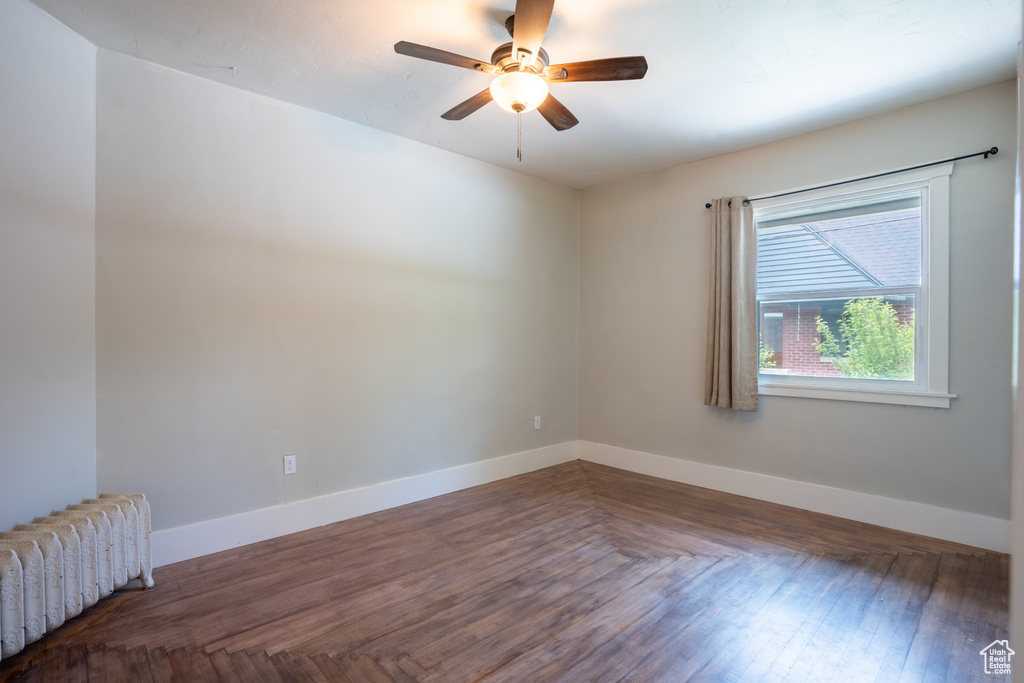 Empty room with radiator heating unit, ceiling fan, baseboards, and wood finished floors