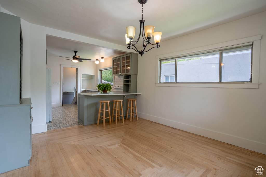 Kitchen featuring baseboards, a peninsula, a chandelier, glass insert cabinets, and a kitchen bar