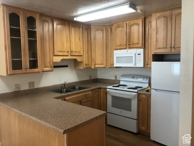 Kitchen with white appliances, a sink, a peninsula, glass insert cabinets, and dark wood finished floors
