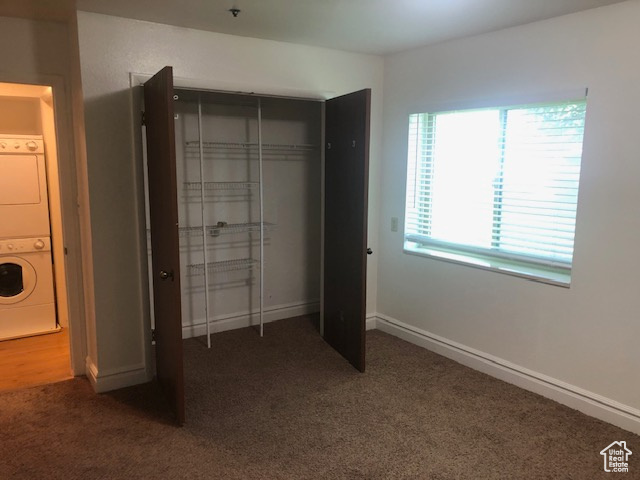 Unfurnished bedroom with stacked washing machine and dryer, carpet, a closet, and baseboards