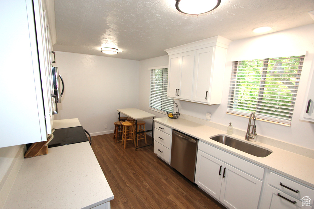 Kitchen featuring dishwasher, a sink, a textured ceiling, light countertops, and white cabinetry