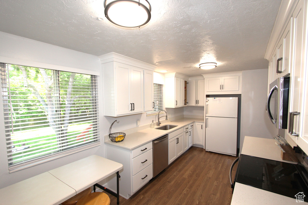 Kitchen with appliances with stainless steel finishes, a sink, light countertops, a textured ceiling, and dark wood-style floors