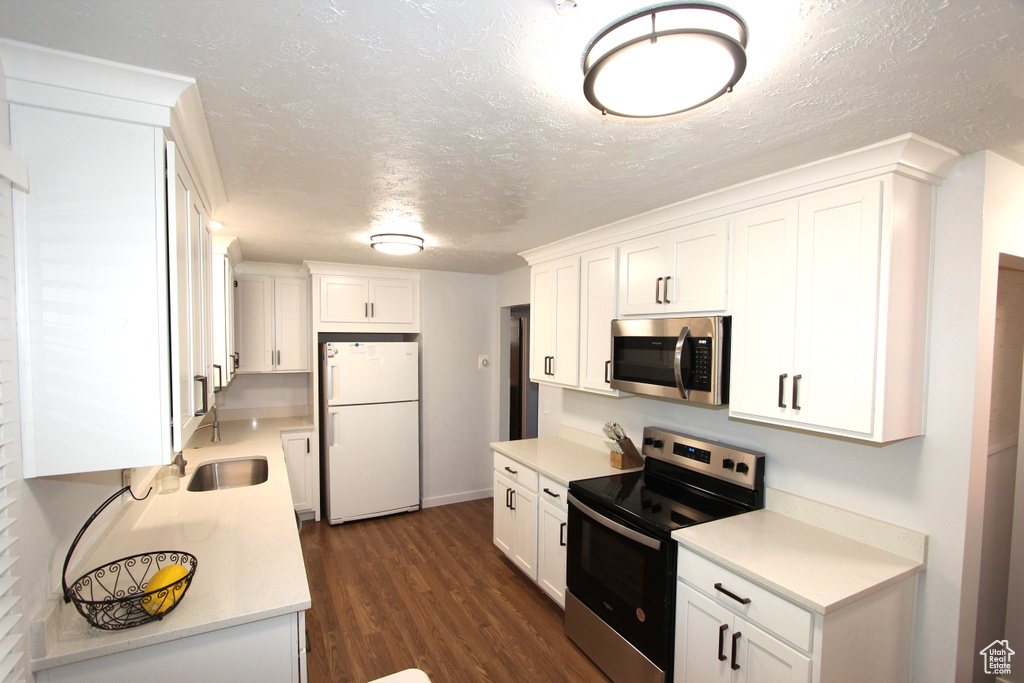 Kitchen with appliances with stainless steel finishes, white cabinets, dark wood-style flooring, light countertops, and a textured ceiling