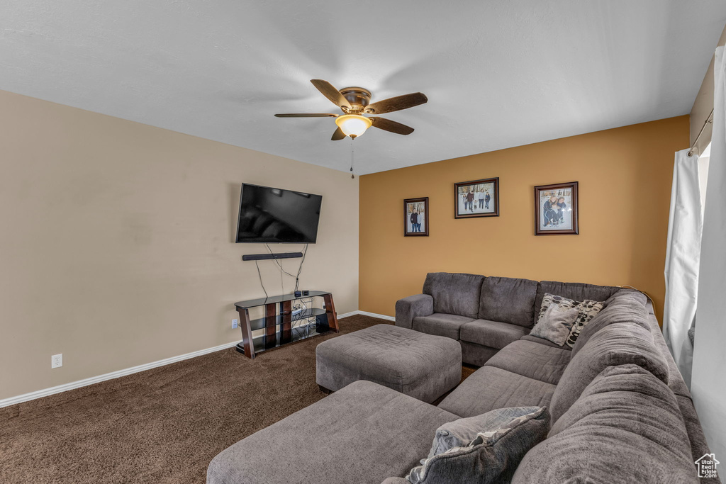 Carpeted living area featuring a ceiling fan and baseboards
