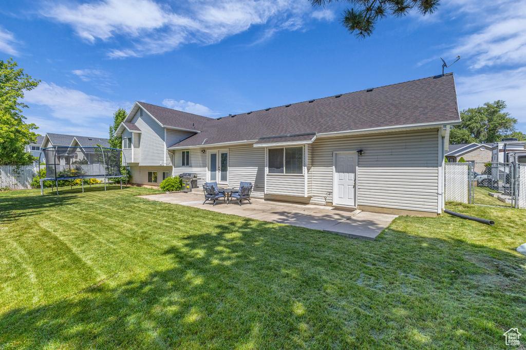Back of property with a trampoline, a patio, and roof with shingles