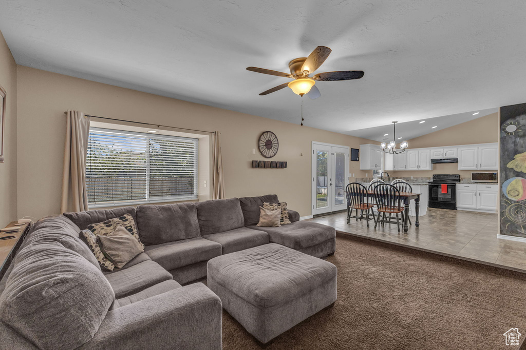 Living room with a chandelier, a ceiling fan, lofted ceiling, light tile patterned floors, and light colored carpet