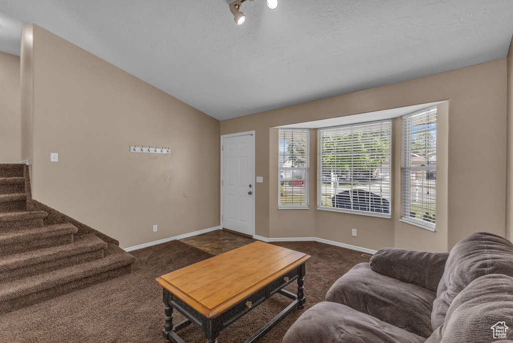 Living room featuring dark colored carpet, lofted ceiling, baseboards, stairway, and a textured ceiling