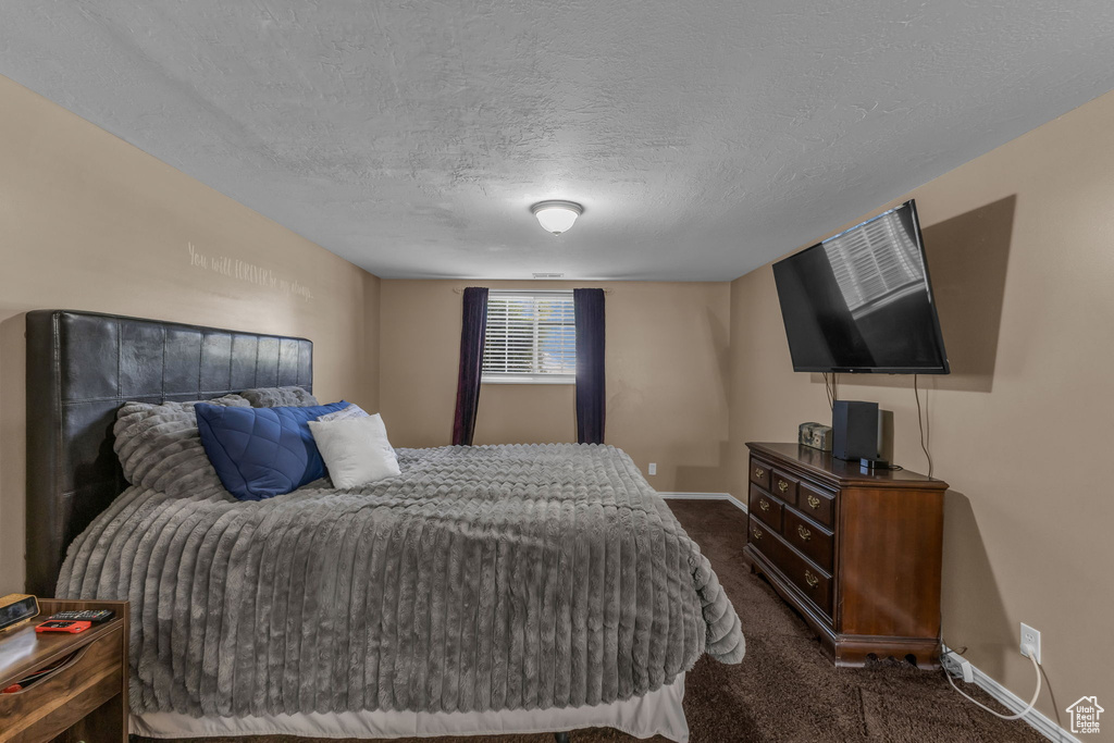 Bedroom featuring dark colored carpet, baseboards, and a textured ceiling