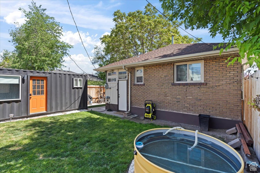 Rear view of property featuring brick siding, an outdoor structure, and a shingled roof