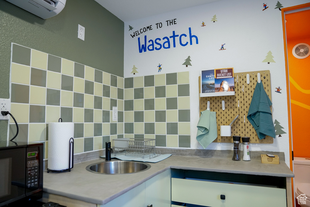 Kitchen with black microwave, a sink, a wall mounted air conditioner, decorative backsplash, and light countertops