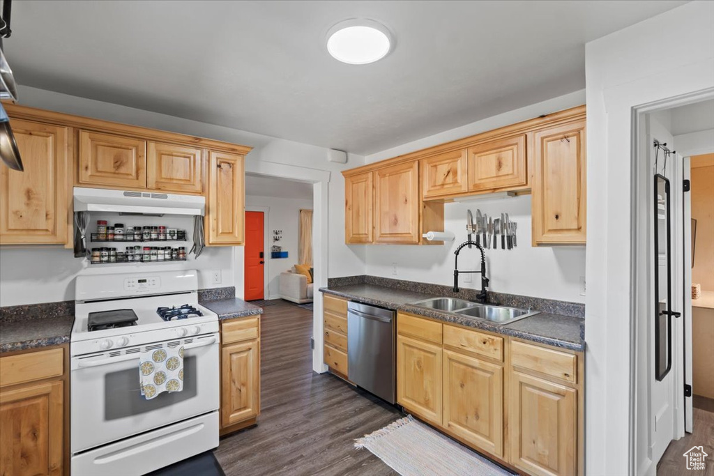 Kitchen featuring white gas range oven, a sink, dishwasher, under cabinet range hood, and dark countertops