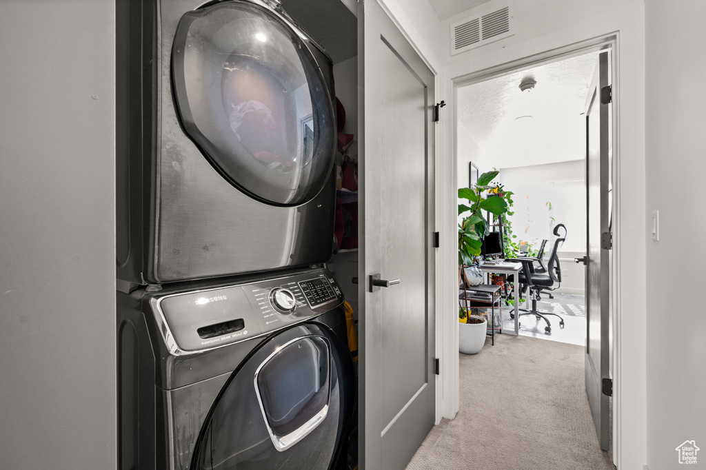 Laundry area with estacked washer and dryer, carpet flooring, and an office area