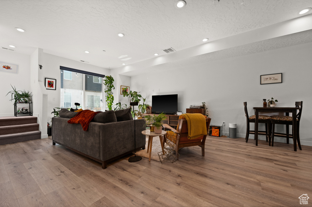 Living room with wood finished floors, a textured ceiling, recessed lighting, baseboards, and stairway
