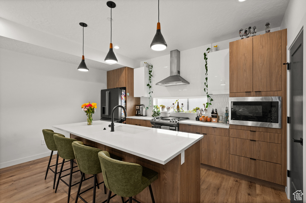 Kitchen with wall chimney range hood, built in microwave, gas stove, a sink, and a breakfast bar area