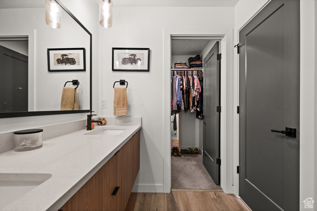 Bathroom featuring double vanity, wood finished floors, baseboards, and a walk in closet