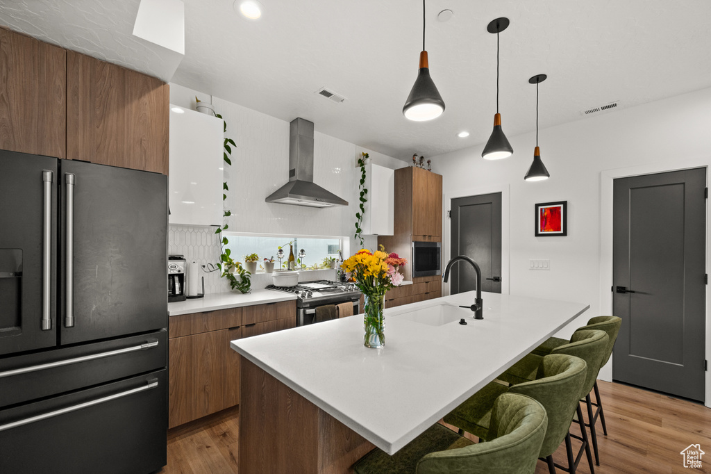 Kitchen with appliances with stainless steel finishes, wall chimney range hood, a sink, light wood finished floors, and recessed lighting