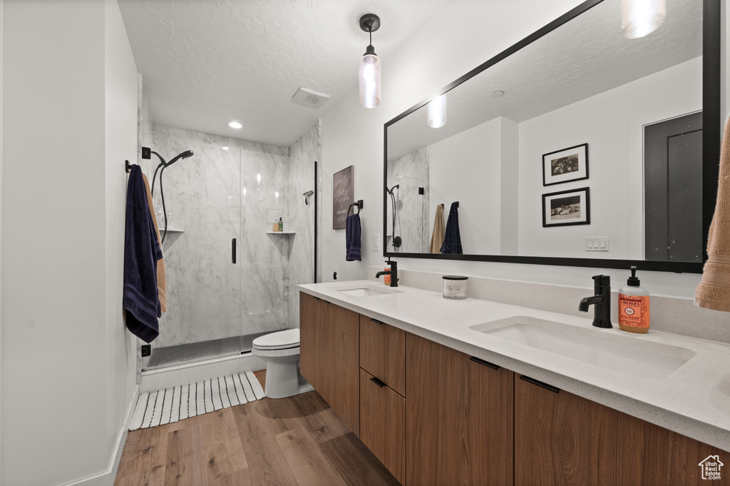 Full bathroom with double vanity, a marble finish shower, toilet, wood finished floors, and a textured ceiling