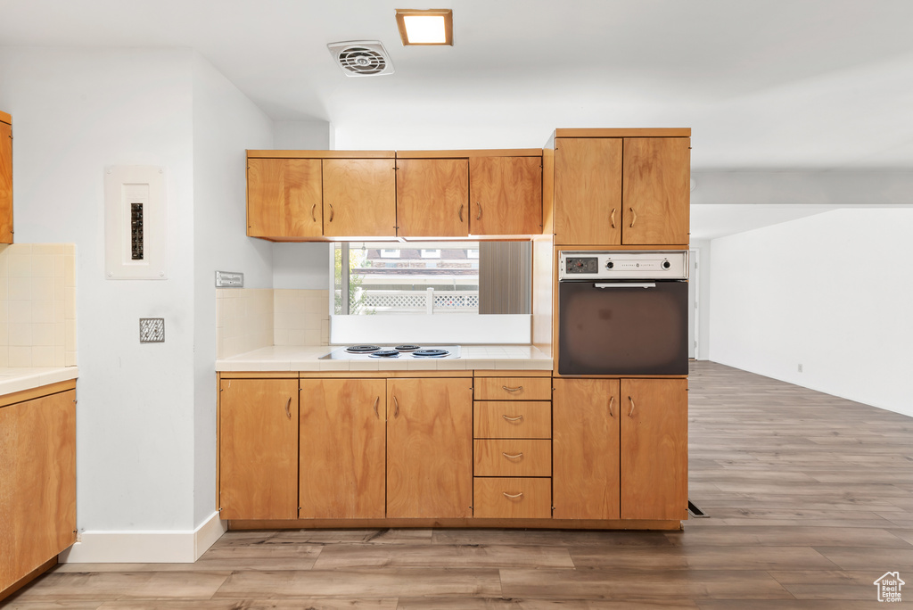 Kitchen featuring oven, light wood-style floors, white electric stovetop, and electric panel