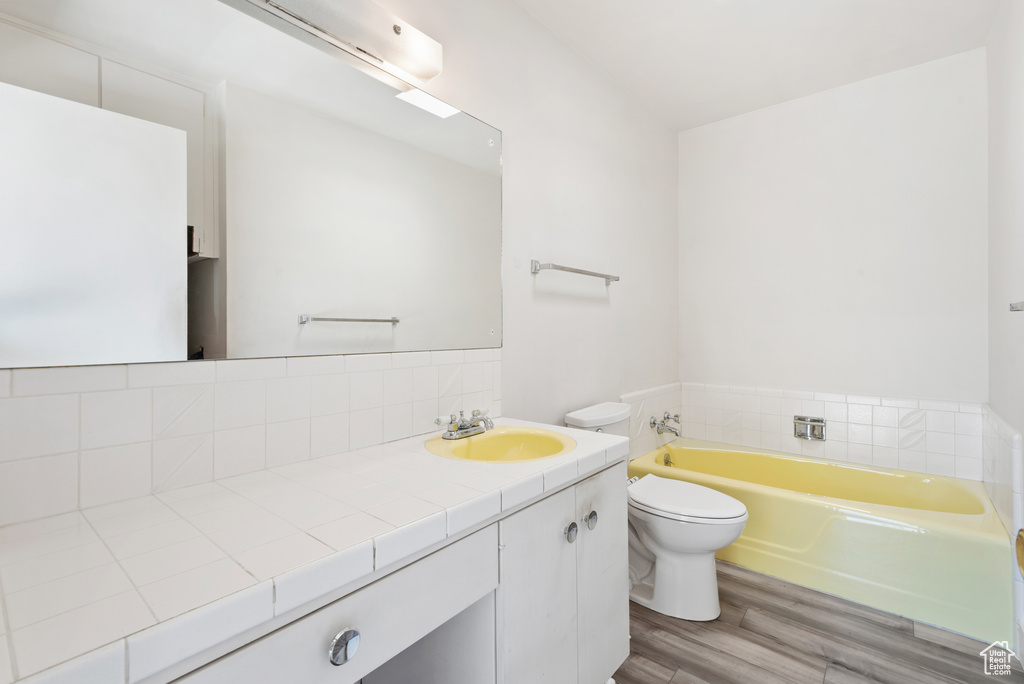 Bathroom featuring a bath, vanity, wood finished floors, toilet, and tasteful backsplash