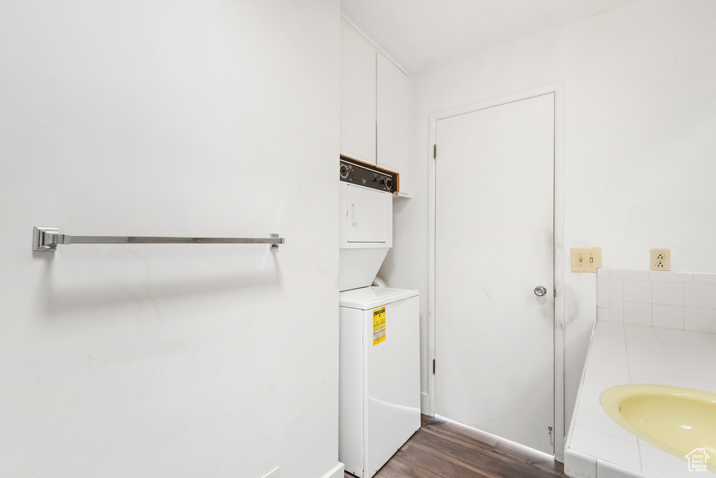 Laundry area featuring stacked washing machine and dryer, dark wood-style flooring, and baseboards