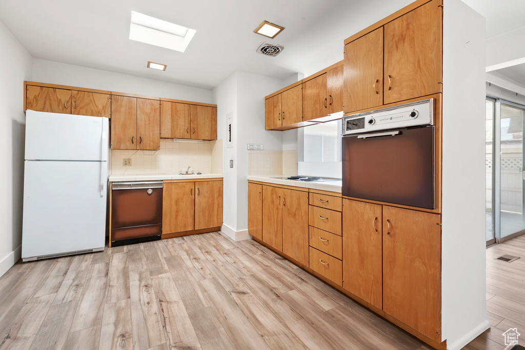 Kitchen featuring freestanding refrigerator, wall oven, dishwasher, a skylight, and light wood-style floors