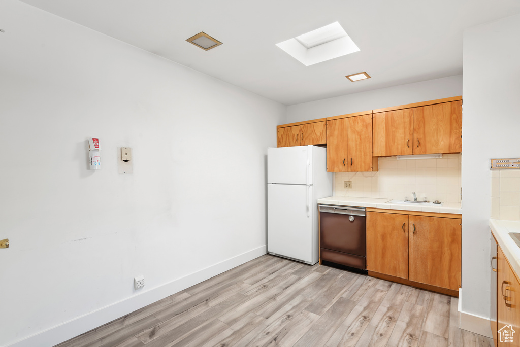 Kitchen featuring freestanding refrigerator, dishwasher, a skylight, light wood-type flooring, and tasteful backsplash