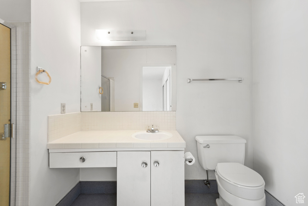 Bathroom with toilet, decorative backsplash, vanity, and a shower with door