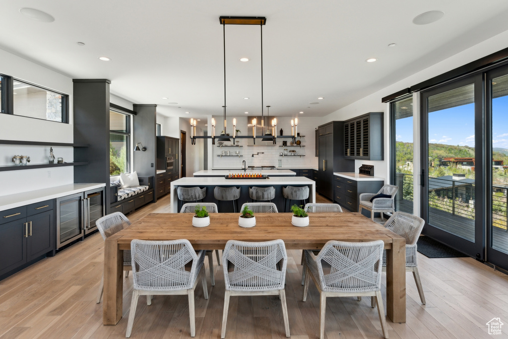 Dining room with plenty of natural light, wine cooler, light wood finished floors, recessed lighting, and a chandelier