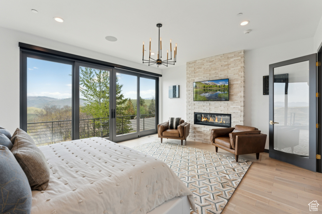 Bedroom featuring access to outside, light wood finished floors, a chandelier, a large fireplace, and recessed lighting