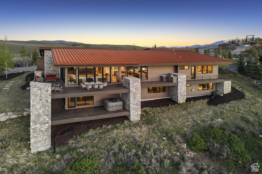 Back of house at dusk with metal roof, a mountain view, a balcony, and stone siding