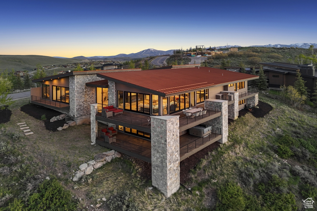 Rear view of property featuring stone siding, a deck with mountain view, and metal roof