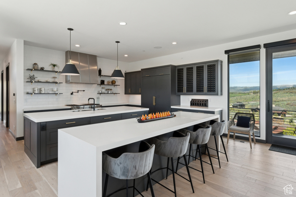 Kitchen with a large island, open shelves, a sink, light countertops, and recessed lighting