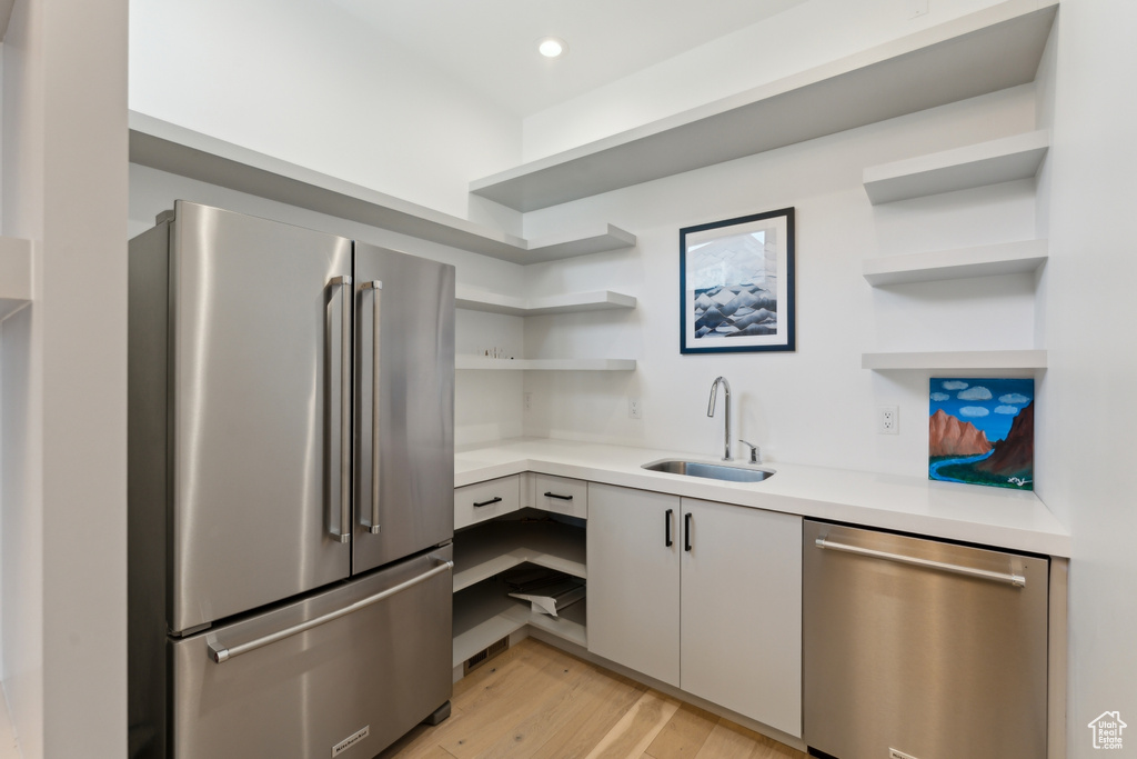 Kitchen with appliances with stainless steel finishes, open shelves, a sink, light countertops, and recessed lighting