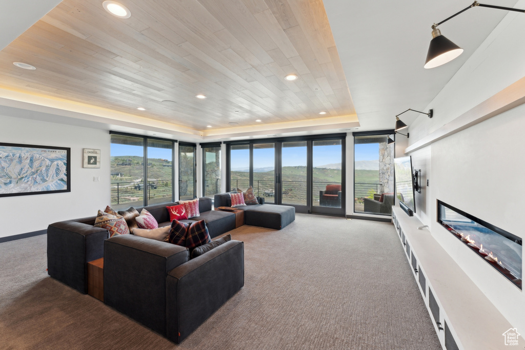 Carpeted living area with a raised ceiling, healthy amount of natural light, recessed lighting, floor to ceiling windows, and wooden ceiling