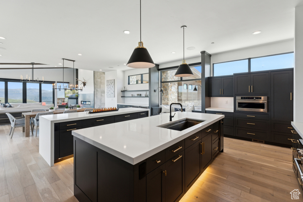 Kitchen featuring a kitchen island with sink, a sink, oven, open floor plan, and light countertops