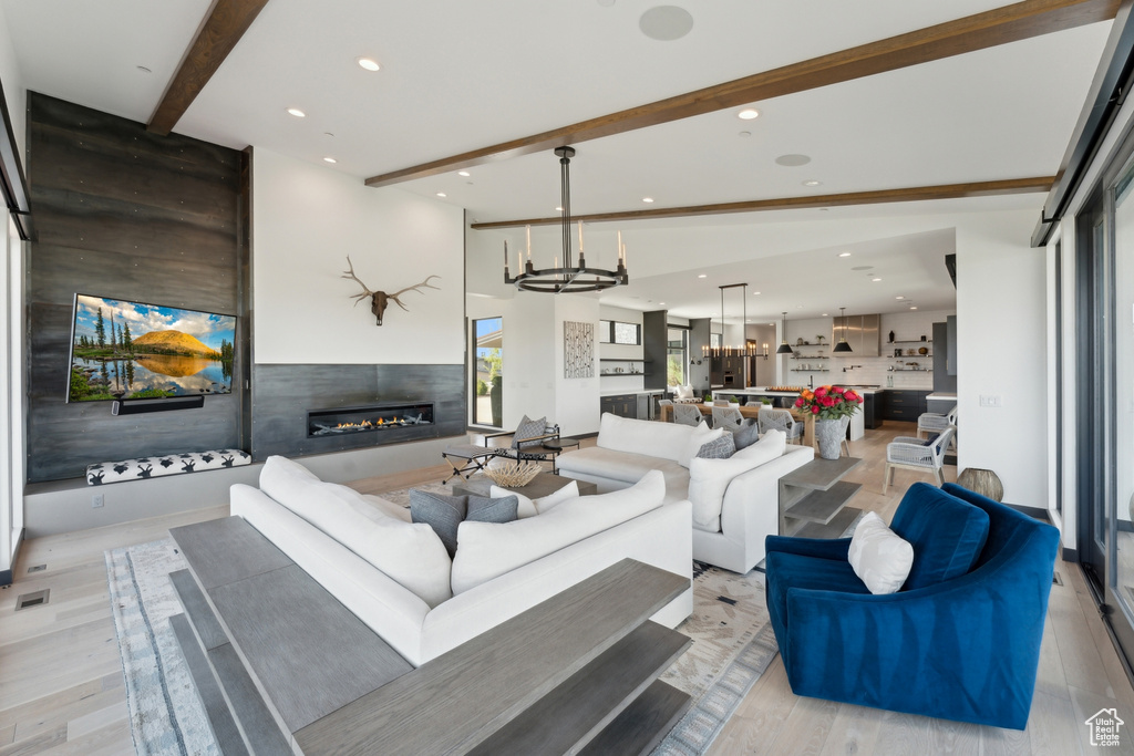 Living room with beamed ceiling, a glass covered fireplace, light wood finished floors, recessed lighting, and a chandelier