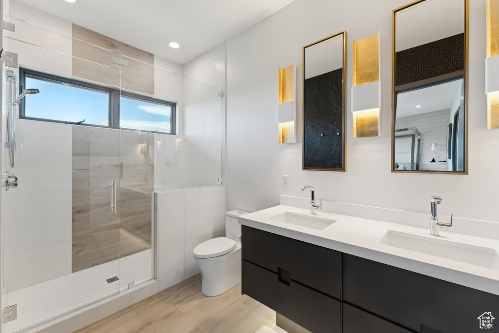 Full bath with double vanity, toilet, a stall shower, wood finished floors, and recessed lighting