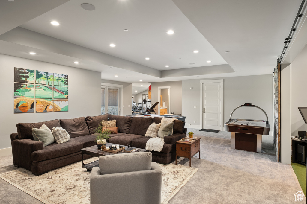 Living area with light colored carpet, recessed lighting, a barn door, a tray ceiling, and baseboards