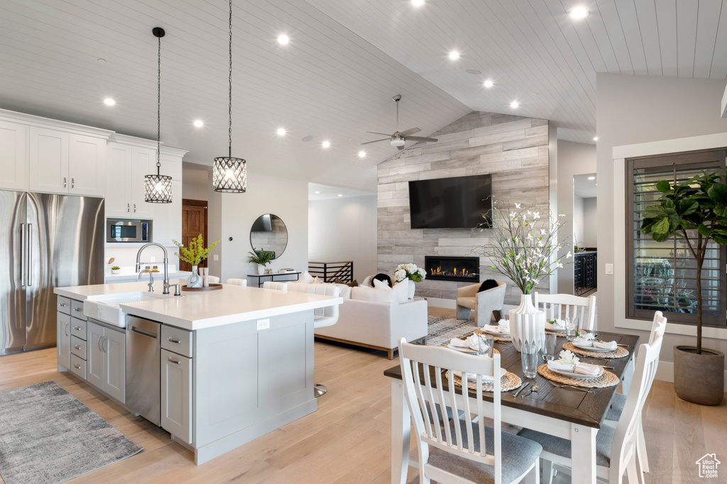 Kitchen featuring appliances with stainless steel finishes, a sink, a tiled fireplace, light countertops, and an island with sink