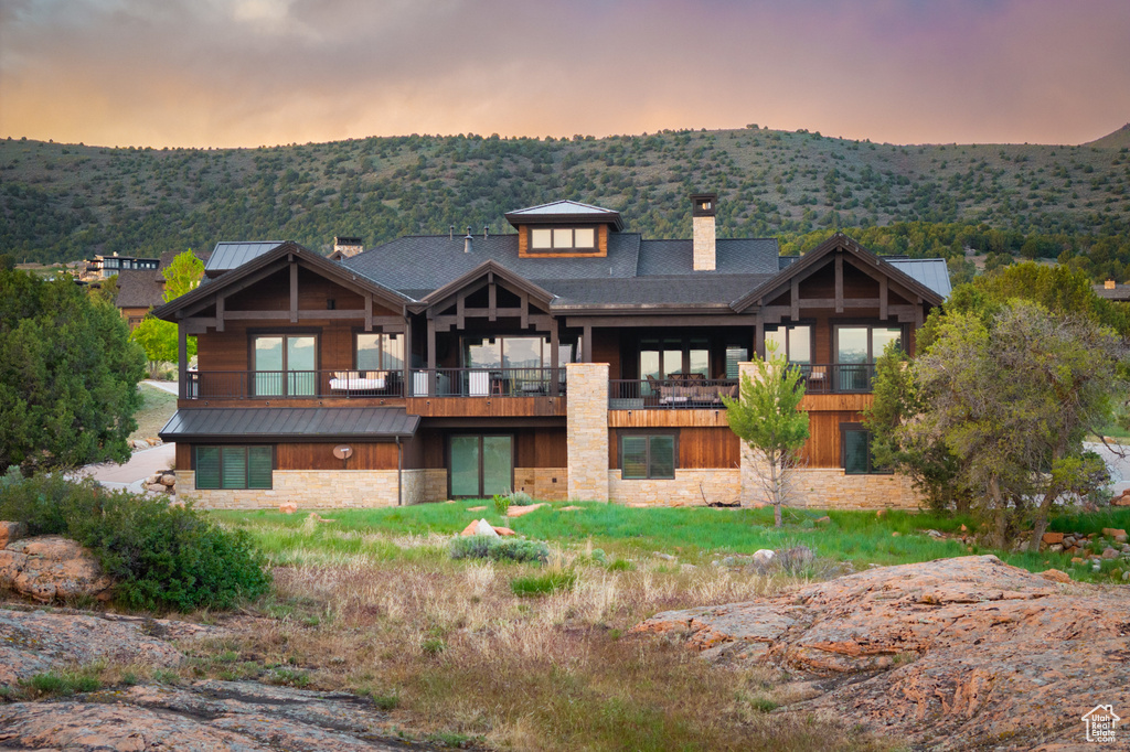 Back of property at dusk featuring a chimney, stone siding, a standing seam roof, and metal roof