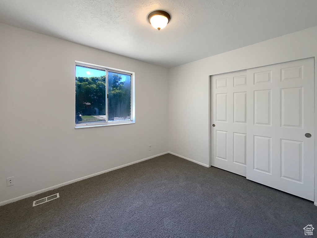 Unfurnished bedroom with dark colored carpet, baseboards, and a closet