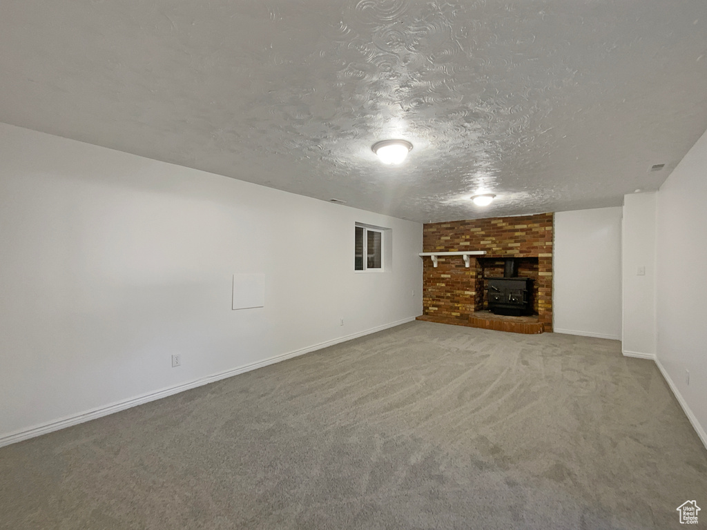 Unfurnished living room featuring a textured ceiling, carpet, baseboards, and a fireplace