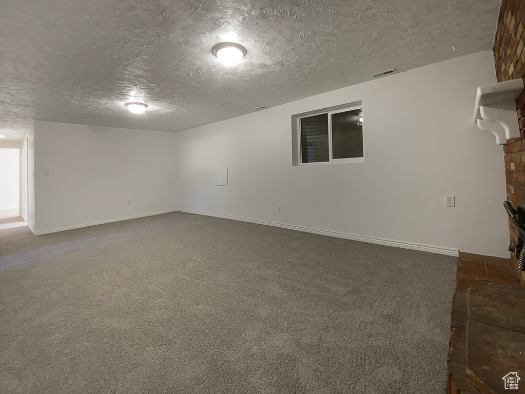 Unfurnished living room featuring a textured ceiling, dark colored carpet, and baseboards