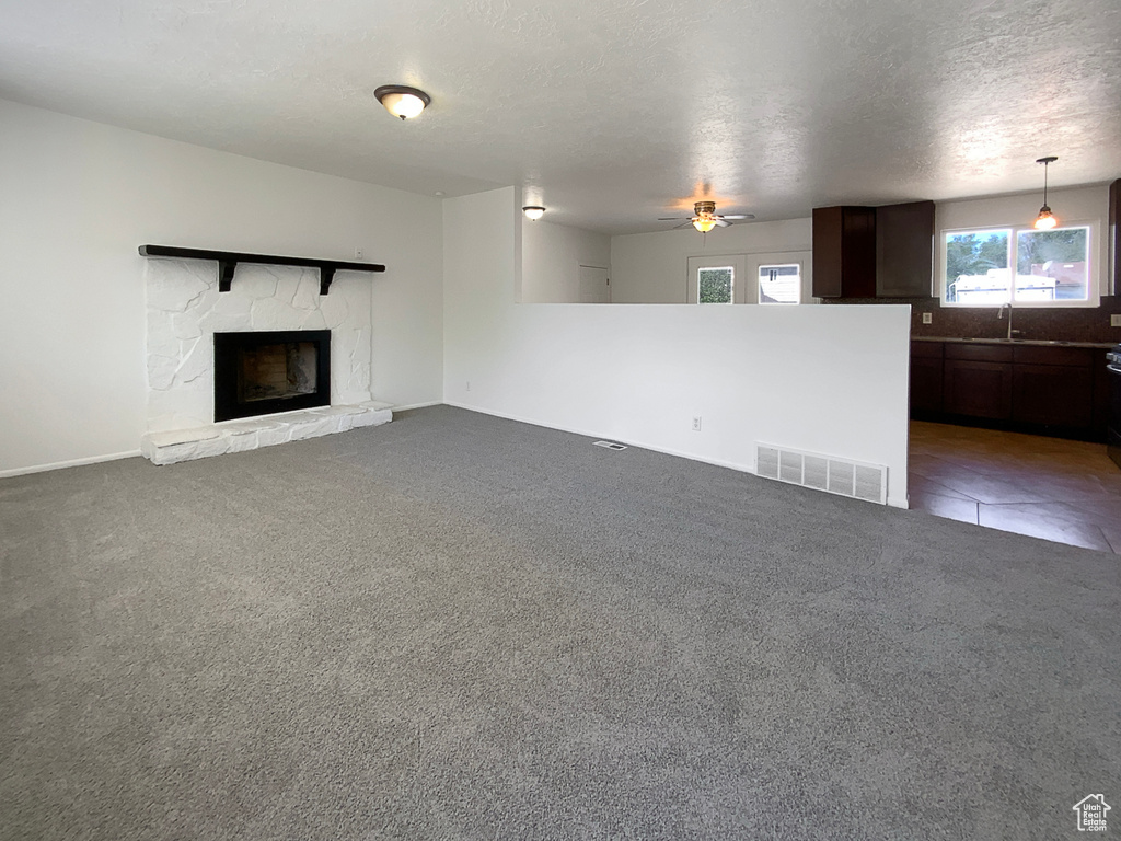 Unfurnished living room with a sink, a stone fireplace, ceiling fan, carpet flooring, and baseboards